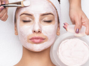 woman getting a pink clay mask applied to her face